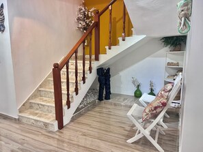 Eine Treppe mit hölzernen Geländern führt zu einer Zwischenebene mit einem weißen Stuhl und einem Tisch.