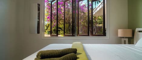 A hotel room with a large bed, a window with a view of pink flowers, and a wall-mounted air conditioner.