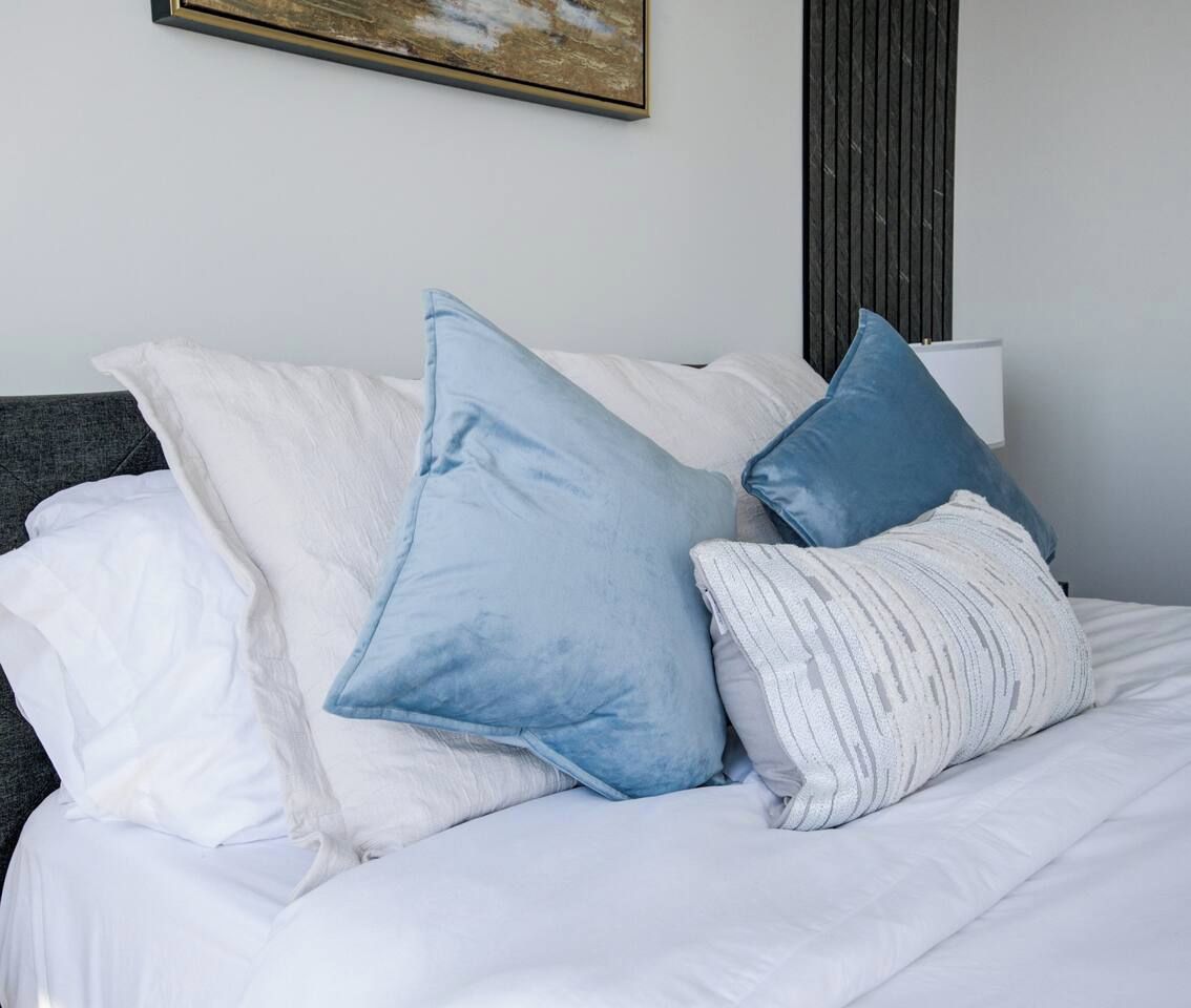 Una cama con ropa de cama blanca y varias almohadas, incluyendo una azul.