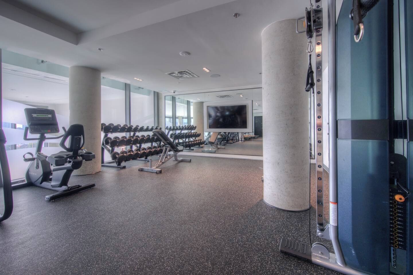 A gym with exercise equipment, a television, and large windows.