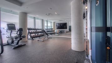 A gym with exercise equipment, a television, and large windows.