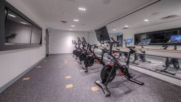 A gym with stationary bikes arranged in a row, a large mirror, and a wall-mounted TV.