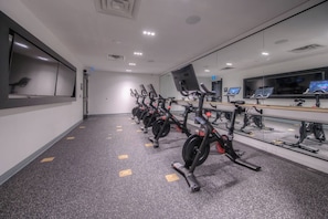 A gym with stationary bikes arranged in a row, a large mirror, and a wall-mounted TV. - Open concept w/ city views (Kitchener)