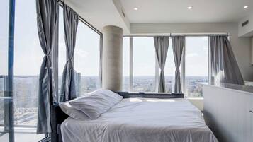 A modern bedroom with a large bed, a view of the city, and a balcony.