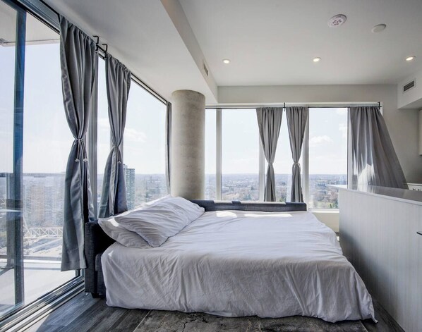A modern bedroom with a large bed, a view of the city, and a balcony. - Open concept w/ city views (Kitchener)