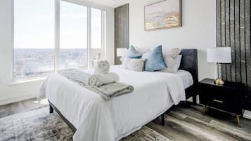 A modern bedroom with a large bed, a nightstand, a lamp, and a city view.
