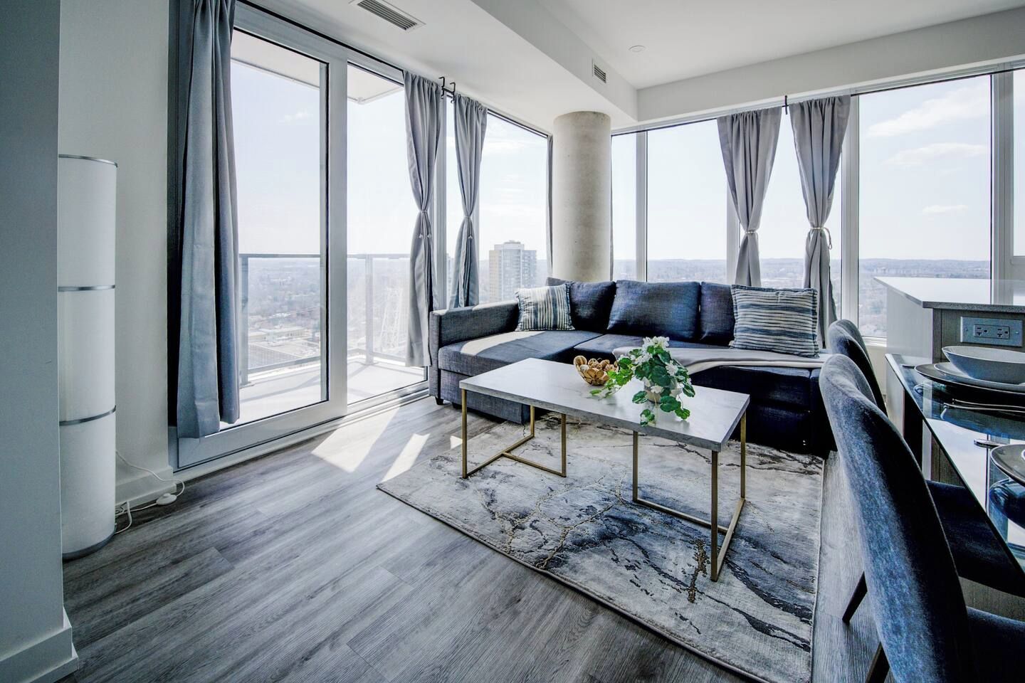 Un salon moderne avec un canapé, une table basse et une vue sur la ville grâce à de grandes fenêtres.