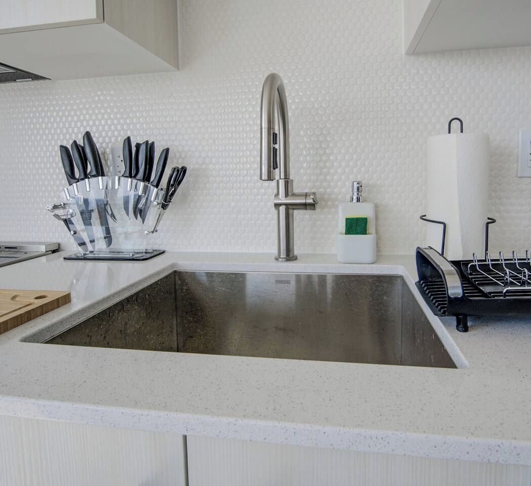 A kitchen with a stainless steel sink, knife block, and paper towel holder.