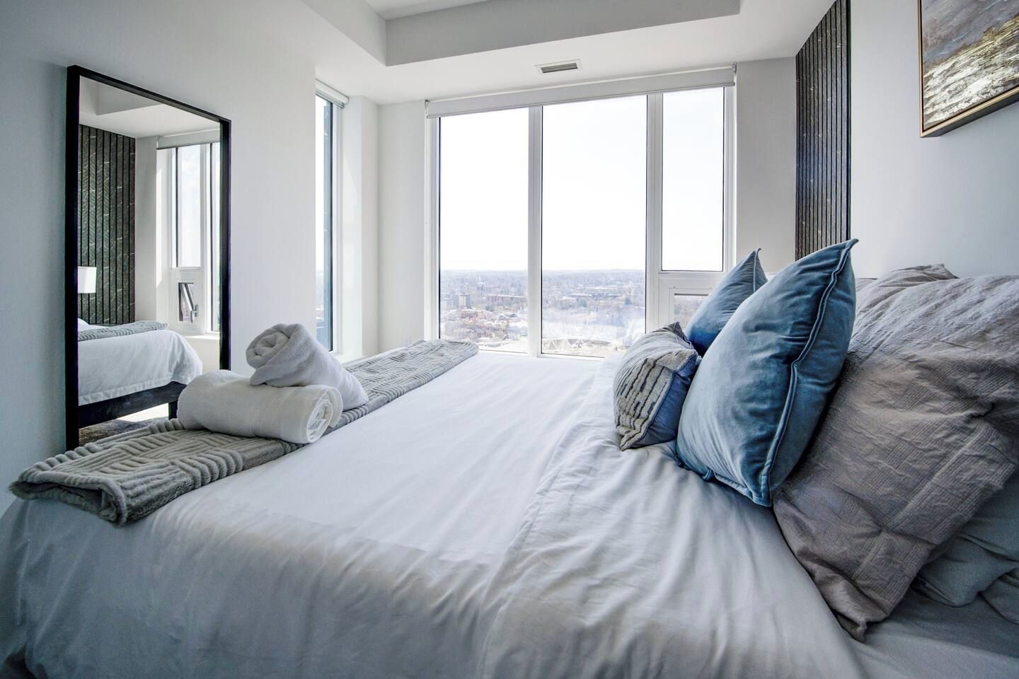 Habitación de hotel con una cama grande, vista a la ciudad y una ventana con persianas.