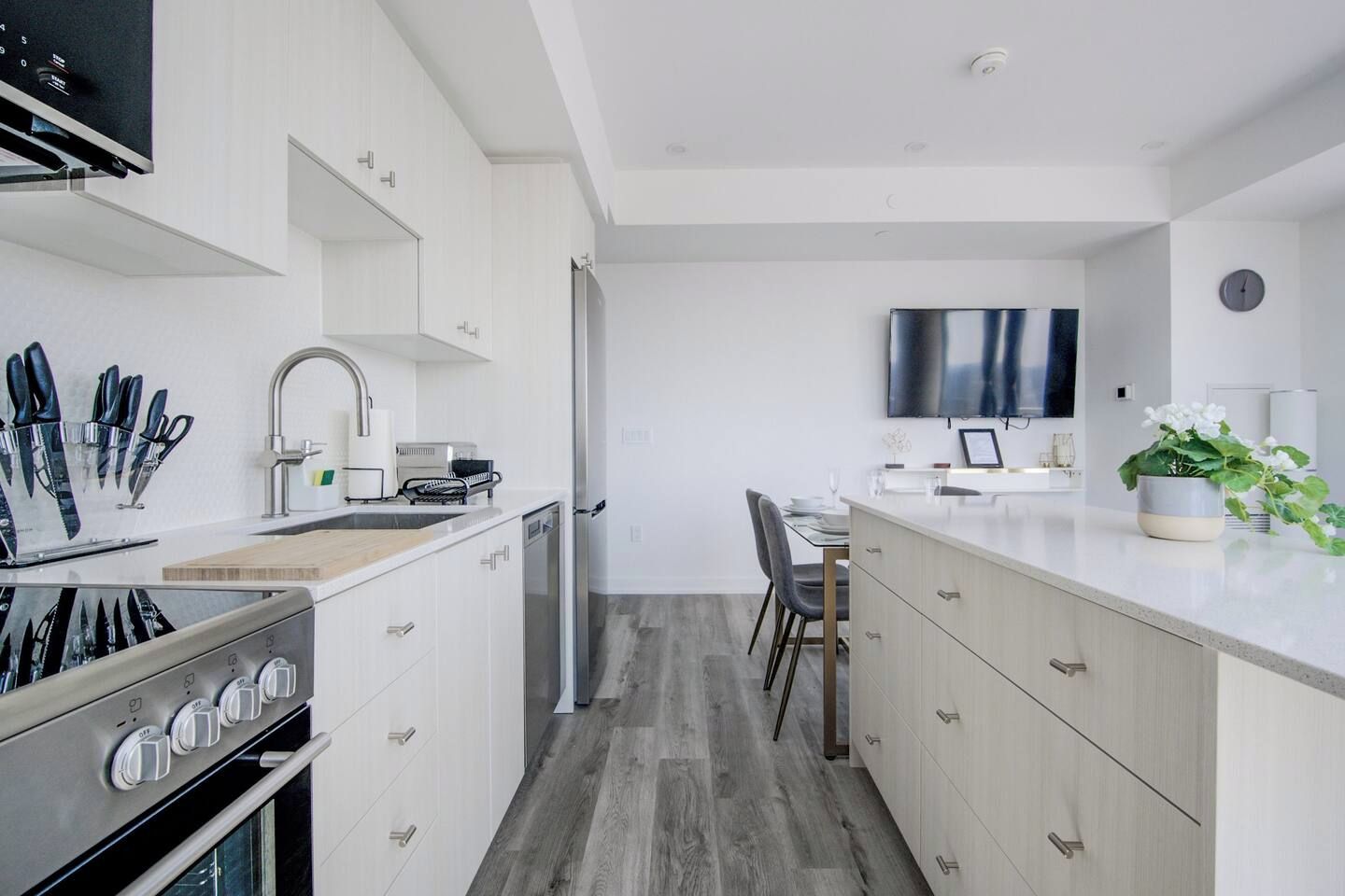 Une cuisine moderne avec des meubles blancs, un four encastré et un coin repas comprenant une table et des chaises.