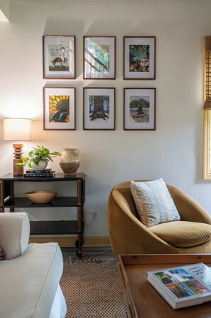 Ein Wohnzimmer mit einer Couch, einem Couchtisch, einer Lampe, einem Bücherregal und einer Wand mit gerahmten Bildern.