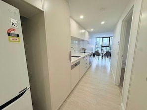 A modern kitchen with a refrigerator, cabinets, and a dining area with chairs and a table. - City Center 1BR丨Steps from Lake丨with Parking (Canberra)