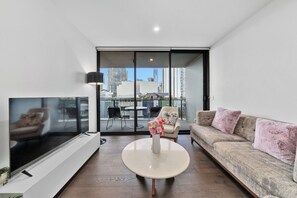 Un salon moderne doté d’un téléviseur à écran plat, d’un canapé, d’une table basse et d’un balcon avec des sièges d’extérieur.