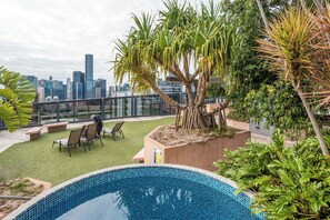 Piscina no terraço com vista para o horizonte da cidade, área de estar ao ar livre e diversas plantas.