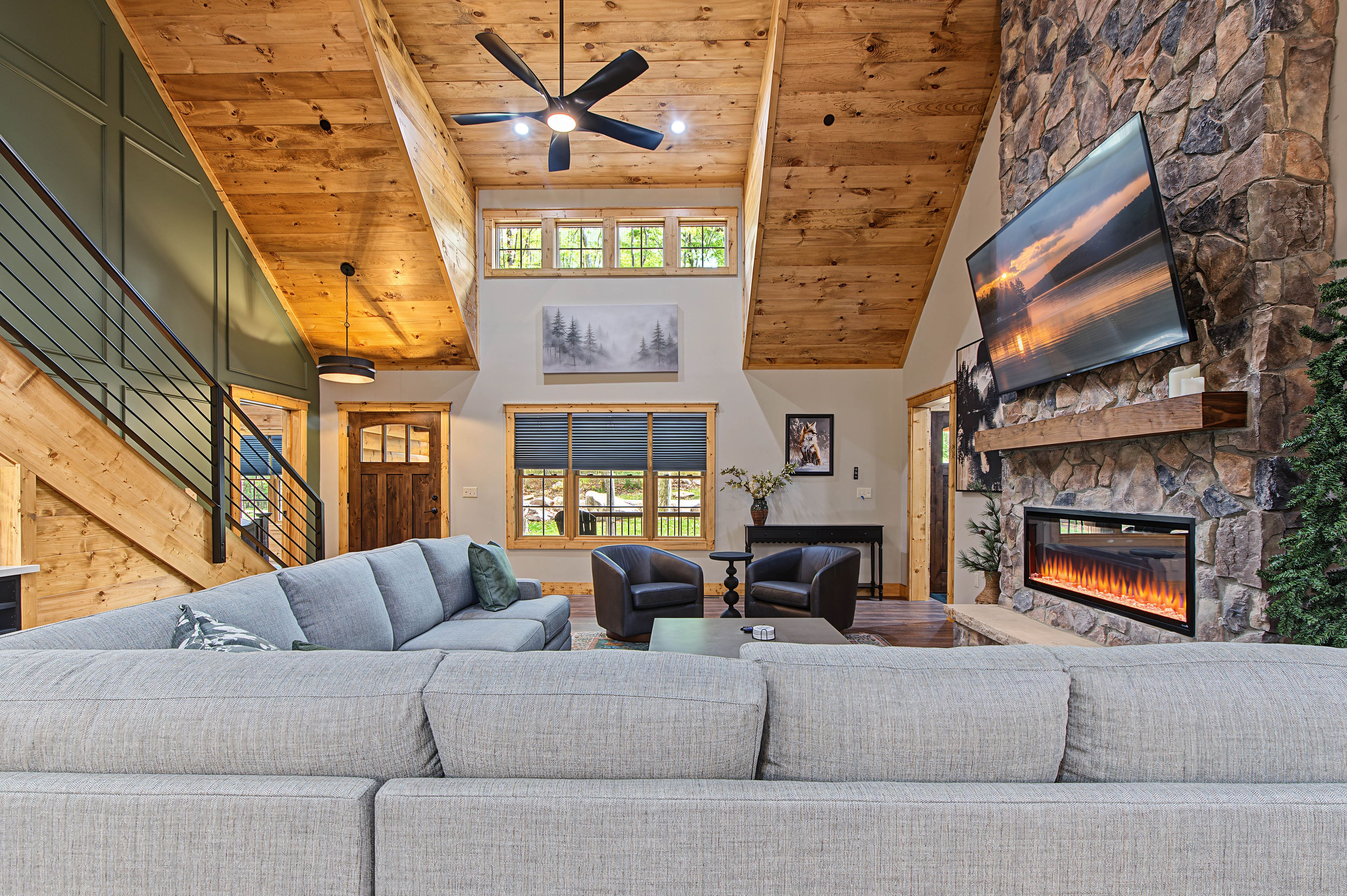 A spacious living room with a fireplace, a large flat-screen TV, and a ceiling fan.