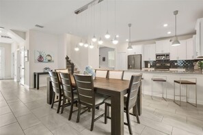 A modern kitchen with white cabinets, a central island, and pendant lighting. - Private Pool & Spa | Six-Bedroom ChampionsGate Home (Kissimmee)