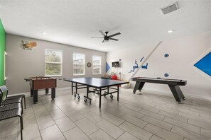 A room with a foosball table, pool table, and a ceiling fan. - Private Pool & Spa | Six-Bedroom ChampionsGate Home (Kissimmee)