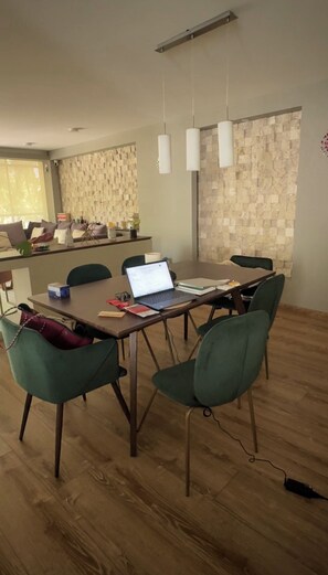 Et moderne spiseområde med et træbord, grønne stole og en bærbar computer på bordet.