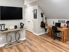 A modern room with a flat-screen TV, a desk with a computer, a guitar, and a sign reading 'MUSCLE SHOALS'.