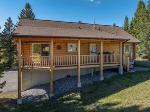 A log cabin with a porch, a chimney, and a window with a curtain. - New! Hiking, Skiing, Biking near Bozeman (Bozeman)
