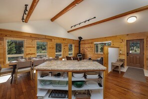 A cozy cabin interior with a dining area, kitchen counter, and large windows. - New! Hiking, Skiing, Biking near Bozeman (Bozeman)