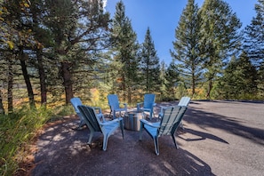 An outdoor seating area with Adirondack chairs and a fire pit surrounded by trees. - New! Hiking, Skiing, Biking near Bozeman (Bozeman)