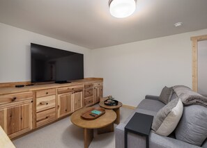 A modern living room with a flat-screen TV, wooden cabinetry, a round coffee table, and a grey sofa. - New! Hiking, Skiing, Biking near Bozeman (Bozeman)