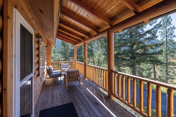 A wooden deck with a view of trees, a covered seating area with a table and chairs, and a wooden railing.