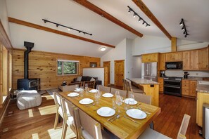 A modern kitchen with wooden cabinets, a dining area with a wooden table set for six, and a built-in wood stove.