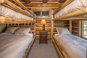 A cabin interior with two bunk beds, a central nightstand with a lamp, and a window. - New! Ski-in/Ski-out, Private Hot Tub, BBQ, Lone Peak! (Big Sky)