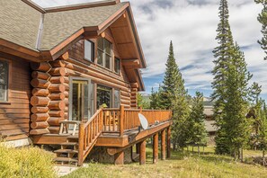 A log cabin with a balcony, a stone foundation, and a mountainous backdrop. - New! Ski-in/Ski-out, Private Hot Tub, BBQ, Lone Peak! (Big Sky)