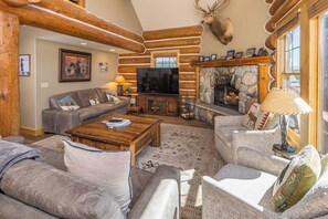 A log cabin interior with a stone fireplace, a television, and a cozy seating area. - New! Ski-in/Ski-out, Private Hot Tub, BBQ, Lone Peak! (Big Sky)