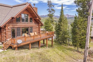 Une cabane en rondins avec une terrasse, de grandes fenêtres et une vue sur les montagnes.