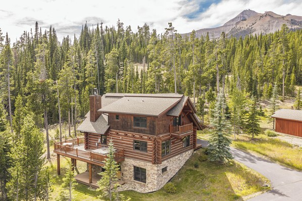 Une cabane en rondins avec des fondations en pierre, une terrasse et une vue sur les montagnes.