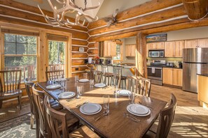L’intérieur d’une cabane en rondins comprend un coin repas, une cuisine et une grande fenêtre donnant sur une forêt.
