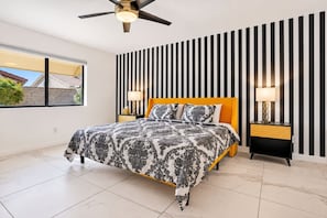 Ein Schlafzimmer mit einem Bett, zwei Nachttischen, einem Deckenventilator und einem Fenster.