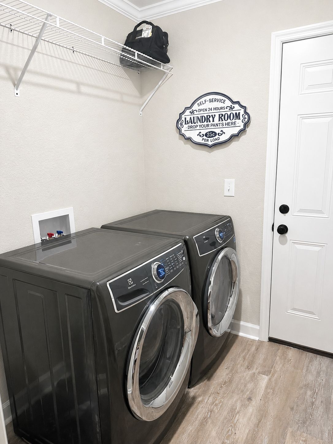 A laundry room with two front-loading washing machines, a drying rack, and a wall sign indicating self-service laundry with 24-hour availability.