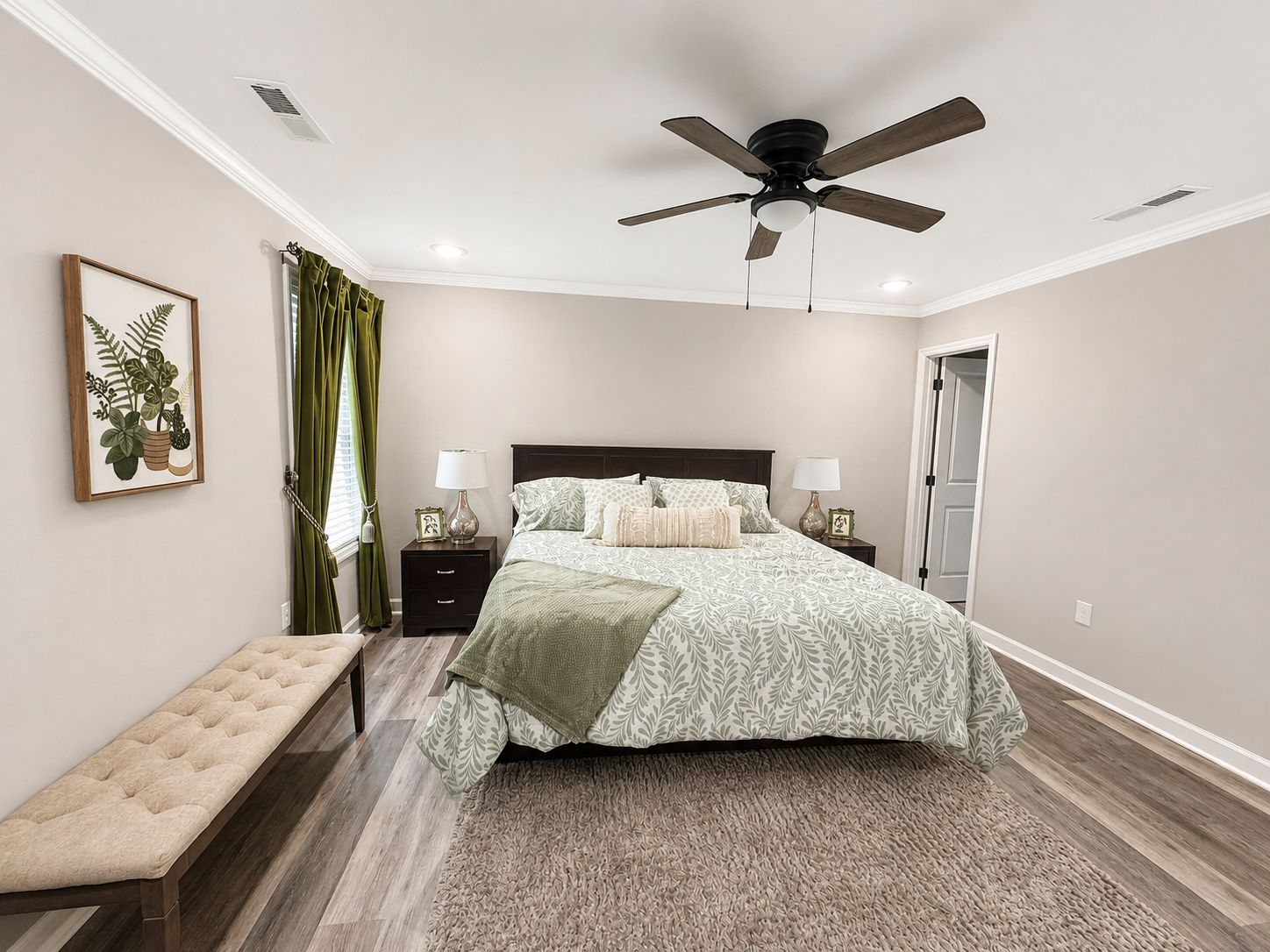A bedroom with a bed, bedside tables, a bench, a ceiling fan, and a framed plant.