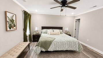 A bedroom with a bed, bedside tables, a bench, a ceiling fan, and a framed plant.