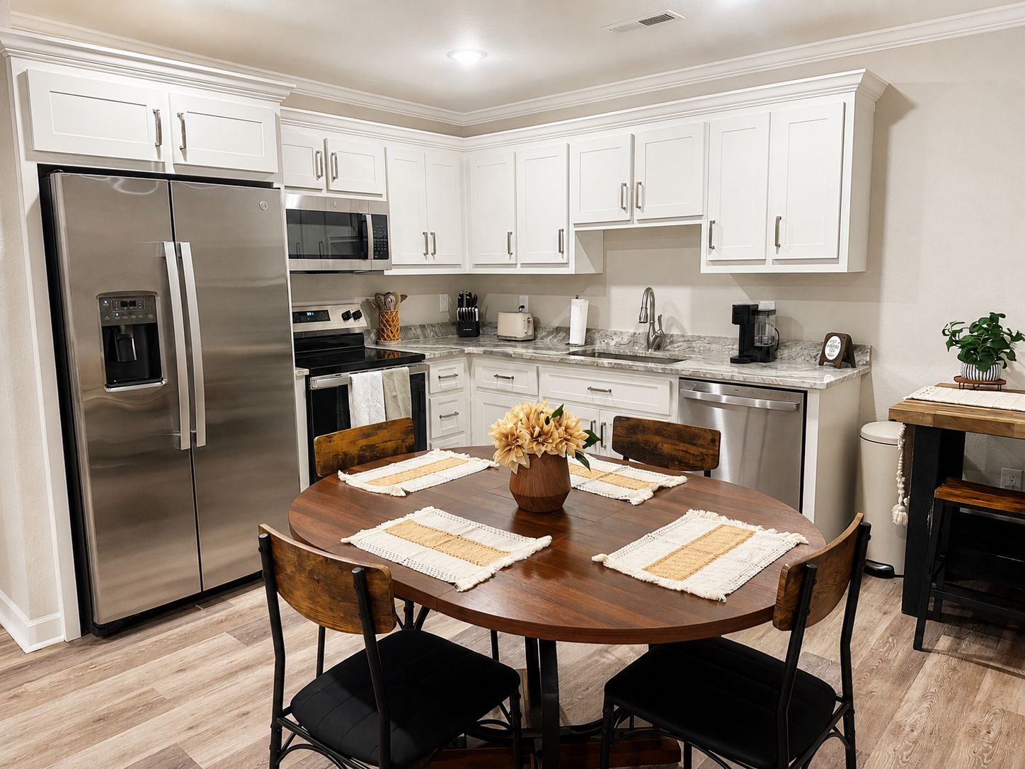 A modern kitchen with white cabinets, stainless steel appliances, and a wooden dining table with chairs.