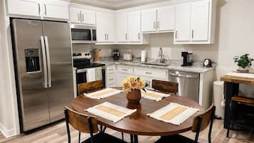 A modern kitchen with white cabinets, stainless steel appliances, and a wooden dining table with chairs.