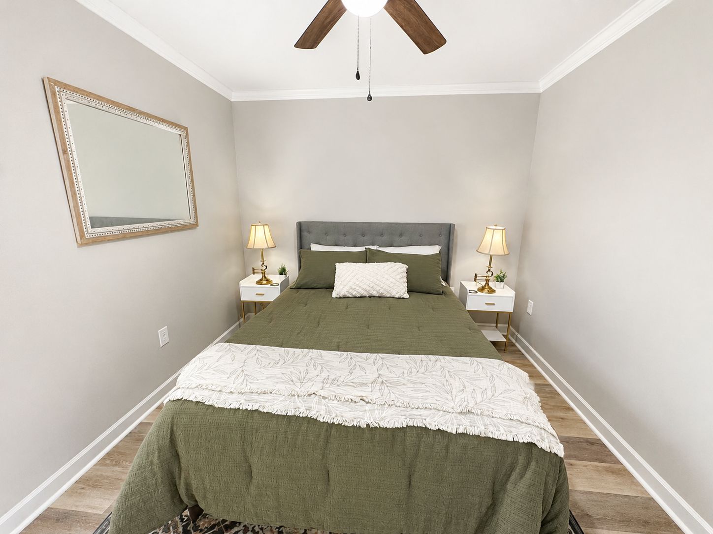 A bedroom with a bed, two bedside tables, lamps, a ceiling fan, and a mirror on the wall.