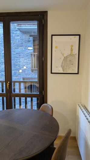 Ein Essbereich mit einem runden Tisch und Stühlen, einem gerahmten Bild an der Wand und Blick durch eine Glastür auf eine steinerne Außenmauer.