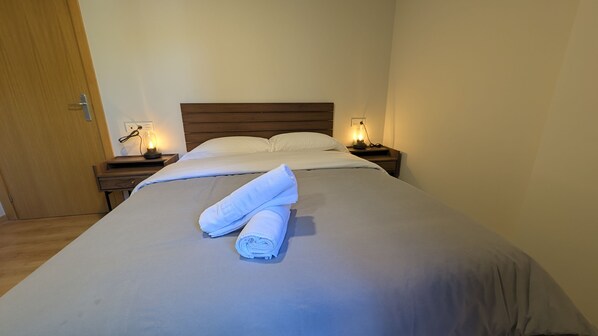 A neatly made bed with a folded towel, two bedside lamps, and a wooden door. - The Little Prince - tucasaenlospirineos (Escarrilla)