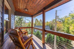 Eine Holzterrasse mit Geländer, eine Veranda mit Blick auf Bäume und Berge sowie zwei Schaukelstühle.