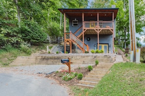 A two-story cabin with a wooden staircase leading to a balcony, surrounded by greenery. - A Cozy Mountain House Near Downtown Banner Elk (Banner Elk)