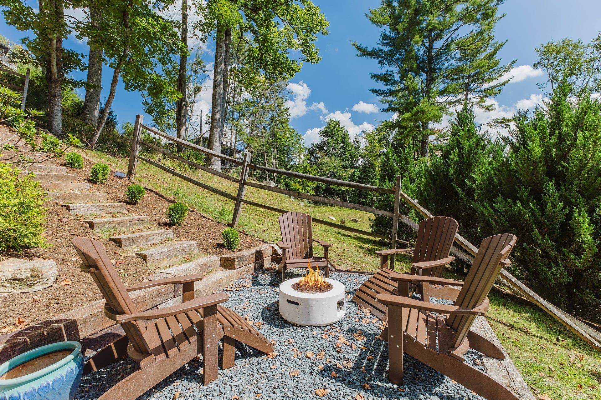 A deck with Adirondack chairs, a fire pit, and a stone staircase leading up.
