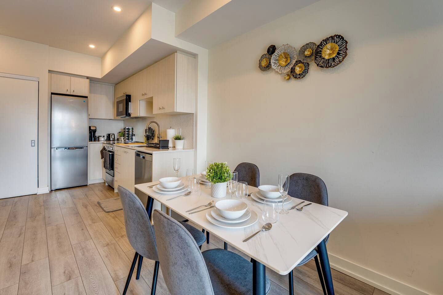 A modern kitchen with a dining area, featuring a stainless steel refrigerator, cabinets, and a dining table set for four.