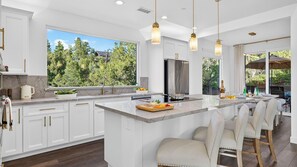 A modern kitchen with white cabinetry, a large island, and a view of trees. - Casa Alta by Avantstay Covered Lounge + Fire Pit + BBQ Red Rock Views (Sedona)