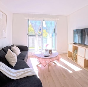 A living room with a sofa, a small round table, a TV, and a balcony with curtains. - Modern Delson Home South Shore Montreal (Delson)